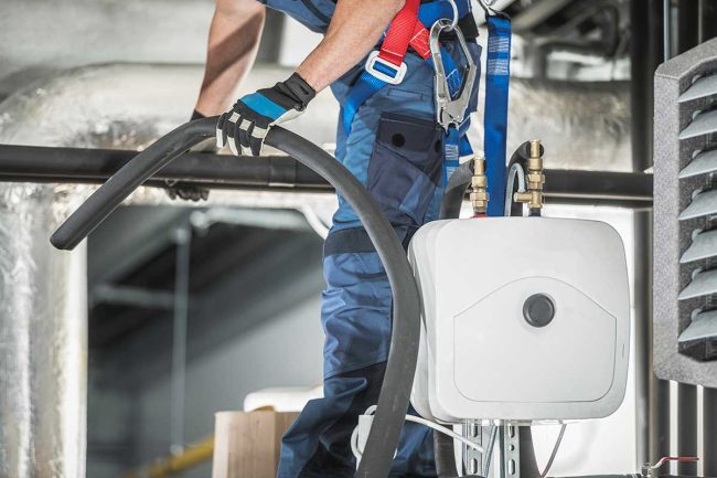 Trabajador realiza mantenimiento aire acondicionado industrial​.